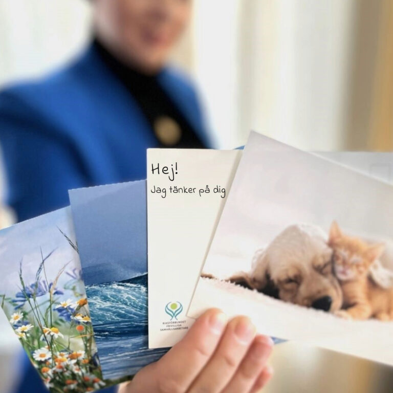 Hand håller i vykort där det står Hej! Jag tänker på dig